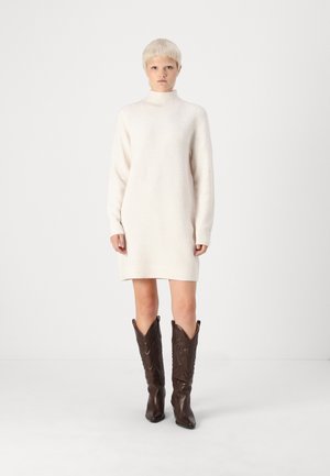 Strikket kjole i off-white, med høy krage og lange ermer. Kombinert med brune skinncowboystøvler med dekorativ søm.