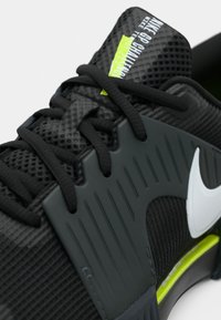 Κοντινή λήψη μαύρου παπουτσιού για τρέξιμο Nike με υφή στα κορδόνια, λευκό λογότυπο Swoosh και ετικέτα "Nike GP Challenge" σε νέον πράσινο χρώμα στη γλώσσα του παπουτσιού.