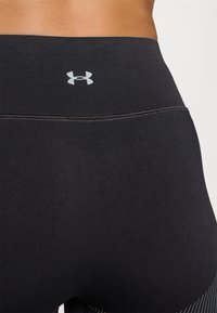 Fekete sport leggings sima textúrával, széles derékrésszel és kicsi szürke logóval a hátsó részen. Diszkrét varrási részlet a tetején.