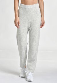 Ljusgrå, mjuka fleece-joggers med resårmidja, tapered ben och minimal texturdetalj. Bärs med vita träningsskor.