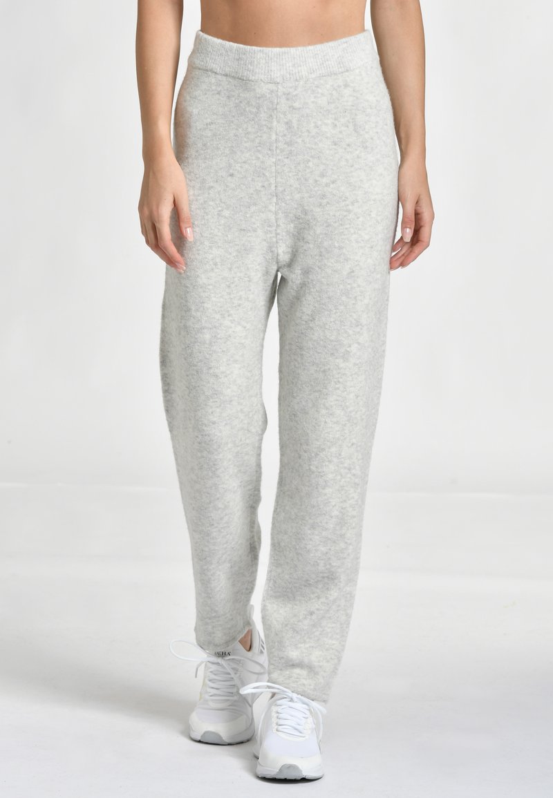 Ljusgrå, mjuka fleece-joggers med resårmidja, tapered ben och minimal texturdetalj. Bärs med vita träningsskor.