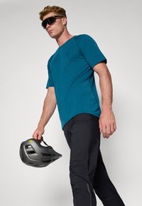 Chemise teal à manches courtes avec un col rond, pantalon noir et casque gris avec des trous de ventilation. Design épuré, textures simples.