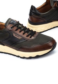 Zapatillas de deporte para hombre con parte superior de cuero marrón oscuro y malla negra, con una suela beige estampada y cordones negros. Logo de la marca visible en el lado.