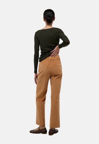 Haut à manches longues côtelé vert foncé associé à un pantalon large en velours côtelé marron clair, avec poches arrière et une finition texturée.