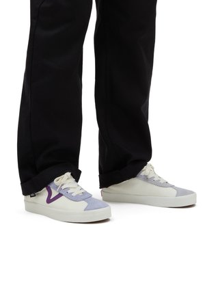 Sneakers Vans con toma in crema, dettagli in suede lavanda e suola in gomma bianca, abbinati a pantaloni neri con orlo arrotolato.