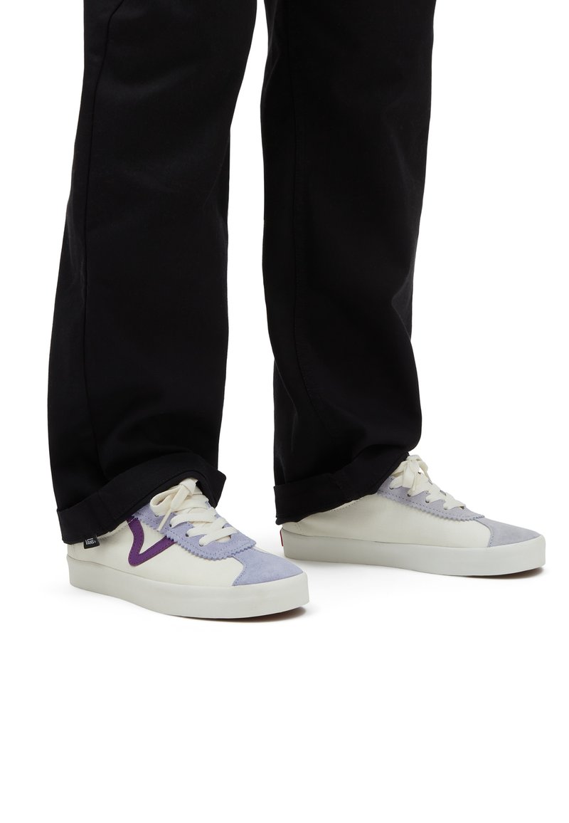 Sneakers Vans con toma in crema, dettagli in suede lavanda e suola in gomma bianca, abbinati a pantaloni neri con orlo arrotolato.