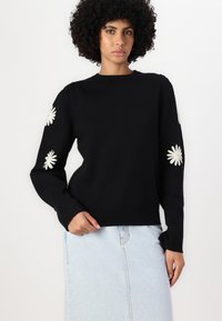 Svart strikkegenser med lange ermer, med kremfarget blomsterbroderi på albuene, rund hals og vanlig passform.