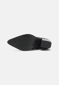 Suela de zapato negra con forma puntiaguda. Presenta una textura de goma suave, sutiles estrías y un pequeño tacón. Diseño elegante y minimalista.