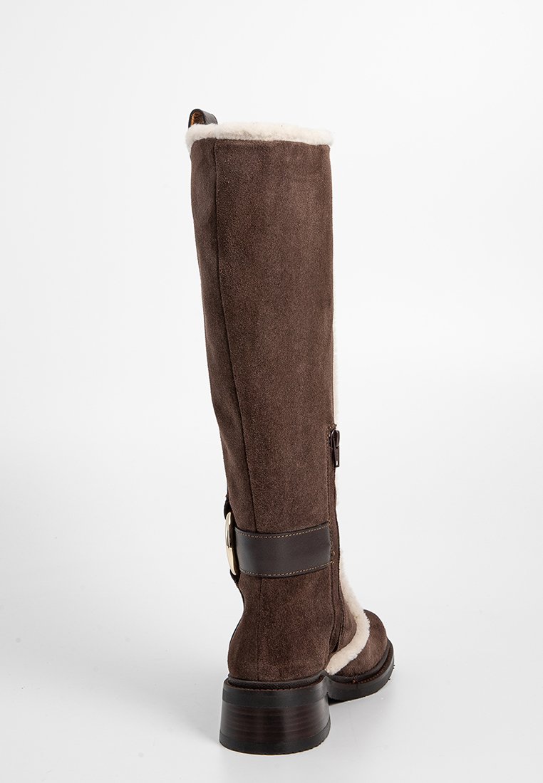 Bruine suède kniehoge laars met shearling voering, leren band en gespdetail, ronde neus en chunky hak. Ritsluiting aan de zijkant.