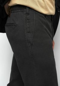 Donkergrijze katoenen broek met een gestructureerde afwerking, voorzien van zijzakken en een elastische taille voor comfort. Top is beige.