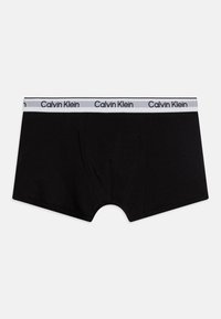 Čierne bavlnené boxerské slipy s bielym elastickým pásom, na ktorom je čiernym písmom vytlačený nápis "Calvin Klein", hladká textúra a priliehavý strih.