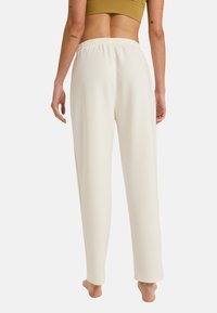Crème kleurige, loszittende broeken met een elastische tailleband en minimale naaddetails, gemaakt van een gladde, zachte stof.