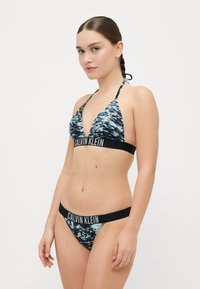 Zwarte en blauwe gemarmerde bikini met een driehoektop en verstelbare bandjes, voorzien van een zwarte band met het "Calvin Klein" logo. Zachte stoftextuur.