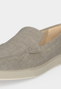 Chaussure décontractée beige à enfiler avec dessus en tissu texturé et semelle en caoutchouc blanche, présentée en gros plan sur un fond uni.