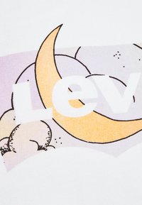 Camiseta de tela blanca con un diseño gráfico colorido que presenta una luna creciente amarilla, un fondo lavanda y un texto en negrita que dice "Levi's."