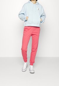 Ljusblå kort hoodie med snörning och ficka; kombinerad med rosa sweatpants och vita högklackade sneakers med svarta accenter.