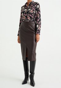 Blommig långärmad skjorta med mörk bakgrund; brun läderkjol med pennform och slits framtill; knähöga svarta spetsiga stövlar.