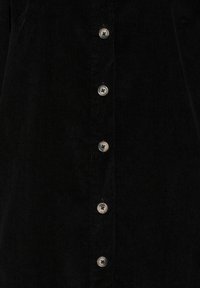 Camicia di velluto a coste nera con una texture a coste verticali e bottoni metallici argentati lungo la parte frontale.