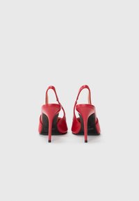 Zapatos de tacón alto de cuero rojo con parte trasera abierta y tira en el tobillo, con un diseño elegante, puntera afilada y tacón negro en contraste.