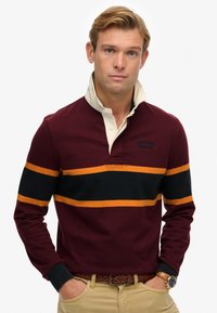 Bordeaux langærmet polo skjorte med en creme farvet krave, prydet med sorte og orange vandrette striber samt broderet logo detaljer på brystet.