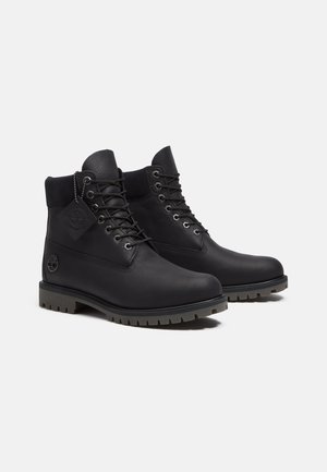 Zwarte leren enkellaarzen met een gestructureerde afwerking, ronde neus, dikke rubberen zolen en een opvallend vetersluting ontwerp. Inclusief een logotag aan de zijkant.