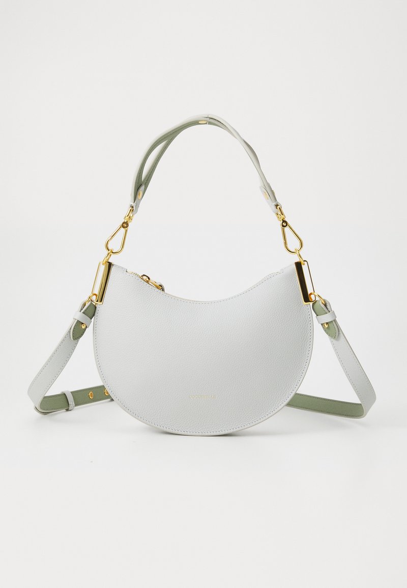 Borsa in pelle grigia chiara con forma a mezzaluna curvata, dotata di accessori in oro, una tracolla verde e superficie texturizzata.