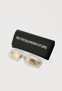 Aurinkolasit kirkkailla kehyksillä ja vaaleanruskeilla linsseillä, mukana musta kotelo, jossa on valkoinen "RETROSUPERFUTURE" -brändäys.