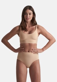 Completo di lingerie color nude, con un bralette morbido e senza cuciture e un perizoma a vita alta. Realizzato in materiale elastico senza cuciture visibili.