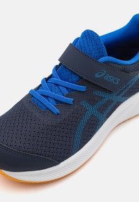 Baskets de sport bleu foncé avec un dessus en maille, des accents bleus et une sangle Velcro. Semelle en caoutchouc avec des détails orange. Présente une couture contrastante.