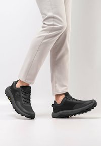 Schwarze Outdoorschuhe mit strukturiertem Synthetik-Obermaterial, robustem Profilsohle und Schnürsenkeln, ausgestattet mit einem Logo an der Seite und einer Zuglasche an der Ferse.