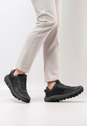 Zwarte buitenschoenen met een gestructureerde synthetische bovenkant, robuuste zool en veters, met een logo aan de zijkant en een trekknoop aan de hiel.