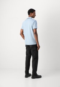 Camisa polo azul claro con ribete negro en el collar, combinada con pantalones cargo negros. El conjunto presenta un corte relajado y un diseño minimalista.
