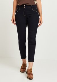 Mörkblå denimjeans med en figursydd design, som har två framknappar, kontrasterande sömmar och uppvikta fållar vid anklarna.