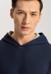 Sudadera azul marino con un forro interior gris, que cuenta con una capucha con cordón y una tela suave y texturizada. Primer plano de la parte frontal.