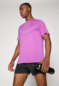 Nike moisture-wicking t-shirt in bright pink, featuring a textured pattern on the chest. Paired with black shorts and a water bottle.