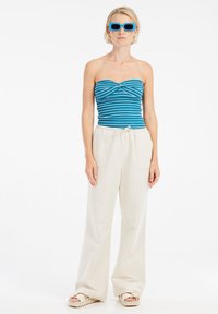 Strapless top in blauw met witte strepen, gecombineerd met crèmewitte wijde broek. Het model draagt blauwe rechthoekige zonnebril en beige sandaaltjes.