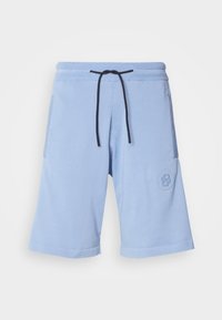 Lyseblå shorts laget av myk stoff. Har en elastisk midjebånd med en svart snor og en logo på side lommen.