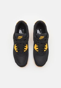 Par svart Nike Air-sneakers med gula detaljer och svarta snören, visade uppifrån på en vit bakgrund.