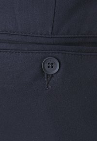 Botón negro cosido en una tela de un oscuro azul marino con el nombre de la marca "ONLY & SONS" grabado alrededor de los ojales.