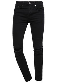 Jeans skinny en denim noir avec déchirures au genou, design à cinq poches, et métal argenté. Présente une silhouette ajustée et un léger stretch.