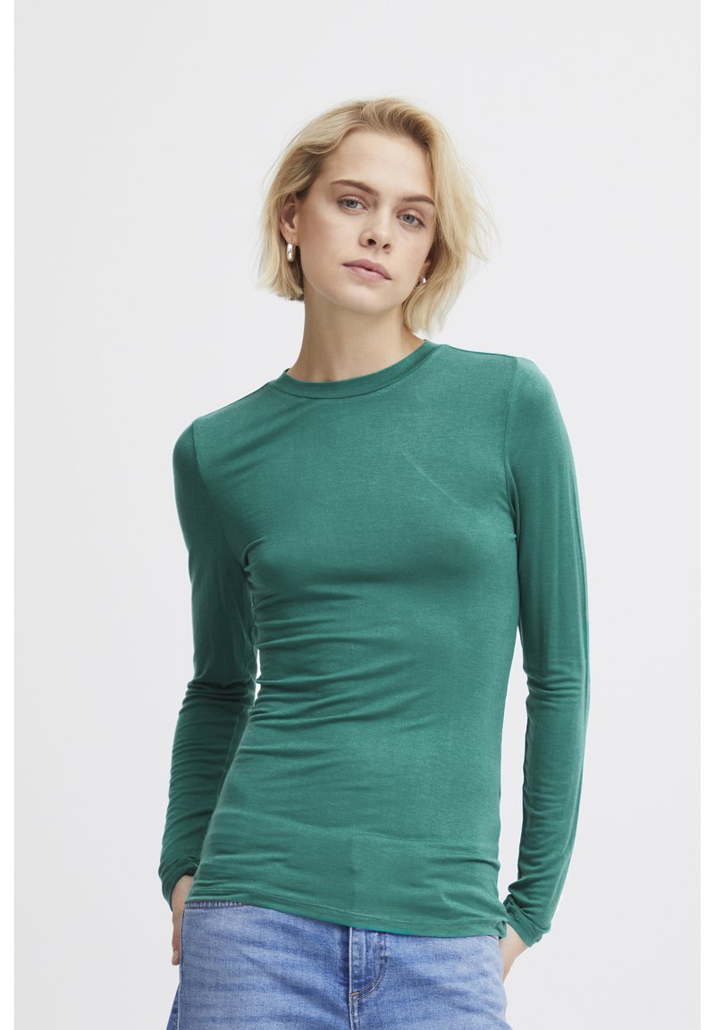 Långärmad grön skjorta i mjukt tyg, med rund halsringning och smal passform som har en mjuk textur. Bärs med blå jeans.