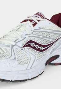 Λευκό και κρασπεδωτό παπούτσι τρεξίματος Saucony με πάνελ από δίχτυ, λευκά κορδόνια, μαλακή σόλα και λογότυπο Saucony στο πλάι και στη γλώσσα.