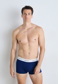 Boxer shorts en coton bleu marine avec une taille blanche arborant le logo "LACOSTE". Texture lisse et design ajusté.