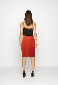 Top de camisolinha em renda preta combinado com uma saia de corduroy ajustada até ao joelho, em tom ferrugem. O conjunto apresenta uma textura lisa e dois bolsos traseiros.