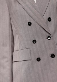 Gray herringbone suit jacket with a double-breasted design, six black buttons, and a side pocket. Textured fabric with vertical stripes.