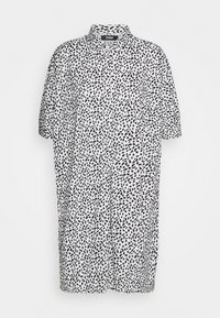 Chemise à manches courtes en tissu léger, avec un motif à pois noir et blanc, un col, et une coupe ample pour le confort.