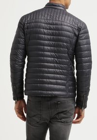 Veste matelassée bleu marine, design matelassé avec des rayures horizontales, matière légère, col montant et poches latérales zippées.