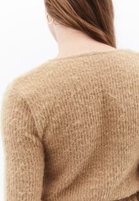 Texturerad ljusbrun tröja med rund halsringning och lös passform. Garnet ser fluffigt ut och ger en mjuk och mysig känsla.