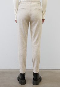Pantalon beige clair à motif chevrons, avec une coupe fuselée, doté de deux poches arrière et porté avec des bottes noires chunky.
