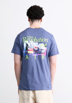Niebieski, bawełniany t-shirt z krótkim rękawem, z nadrukiem graficznym przedstawiającym sneakersy i tekstem "THE Revolution of AIR" w żywych żółtym i fioletowym kolorze.